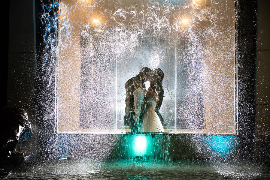 Silhouette of bride and groom behind a lighted waterfall