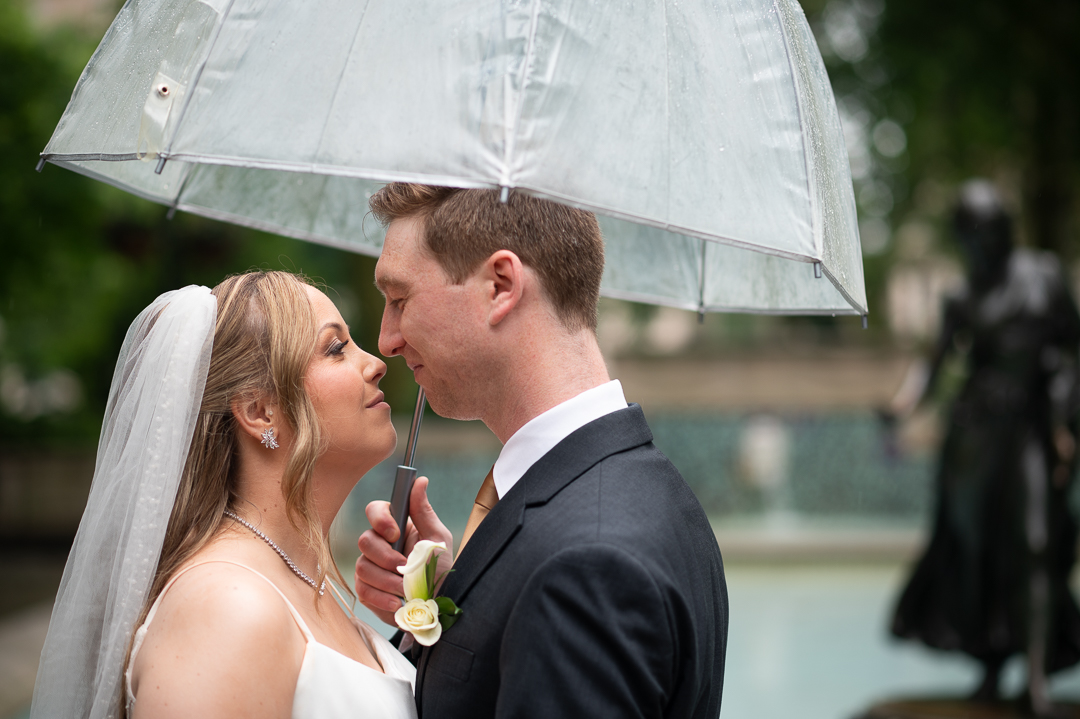 bride and groom smiling at each other outside under a clear umbrella on their spring wedding day